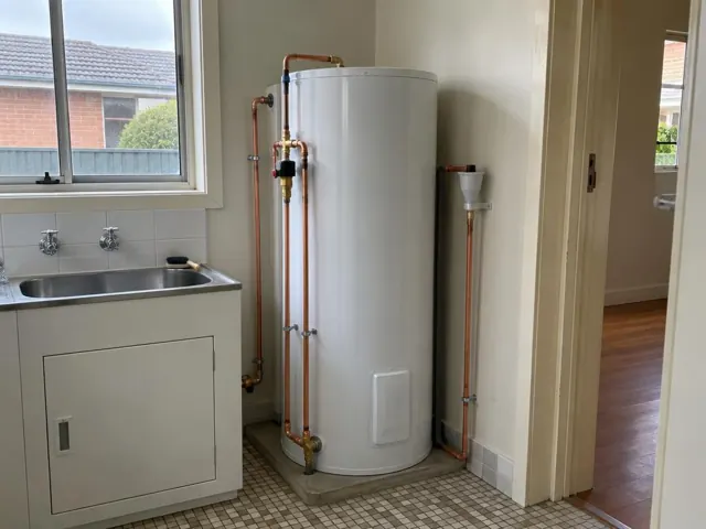 New hot water cylinder beside a laundry sink with copper pipework and tiled floor in Wallsend
