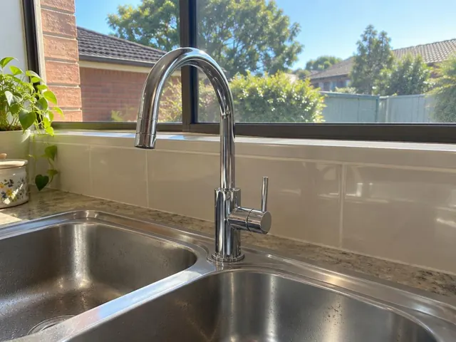 Chrome kitchen mixer tap beside a stainless double sink with tiled splashback and window in Maryland